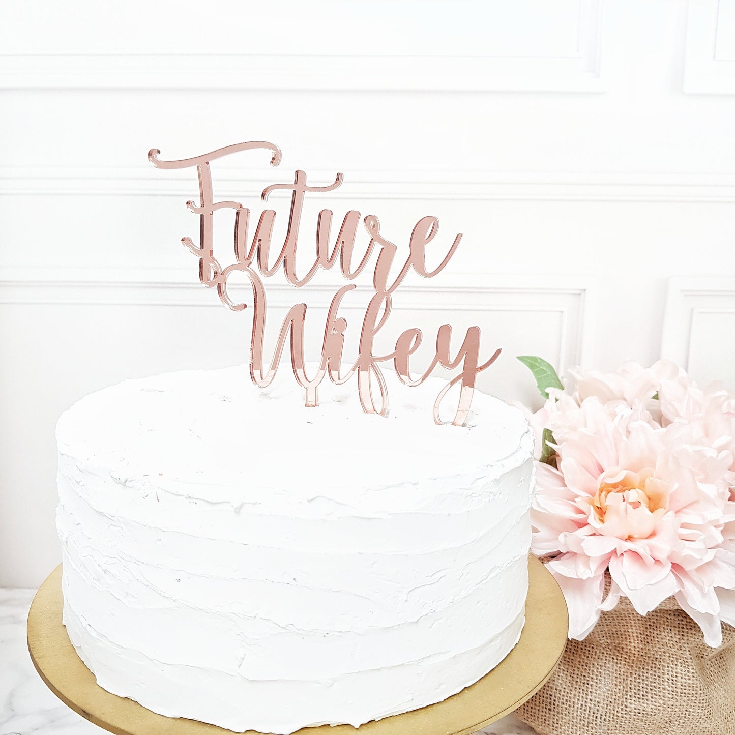 May include: A white cake with a rose gold cake topper that says "Future Wife" in a cursive font.